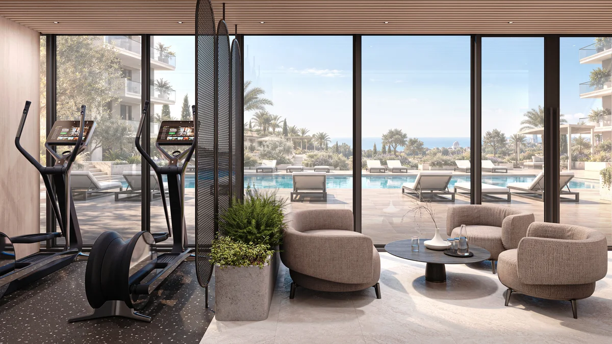Gym cardio equipment and lounge seating beside windows overlooking the swimming pool.